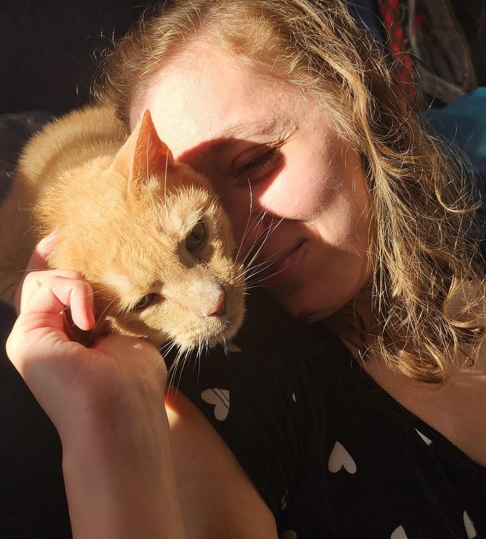 A woman is petting an orange cat who is nuzzling her face.