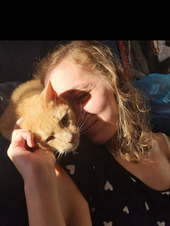 A woman sits with a white golden doodle in her lap and smiles.
