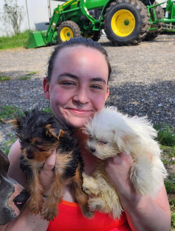 A woman sits with a white golden doodle in her lap and smiles.