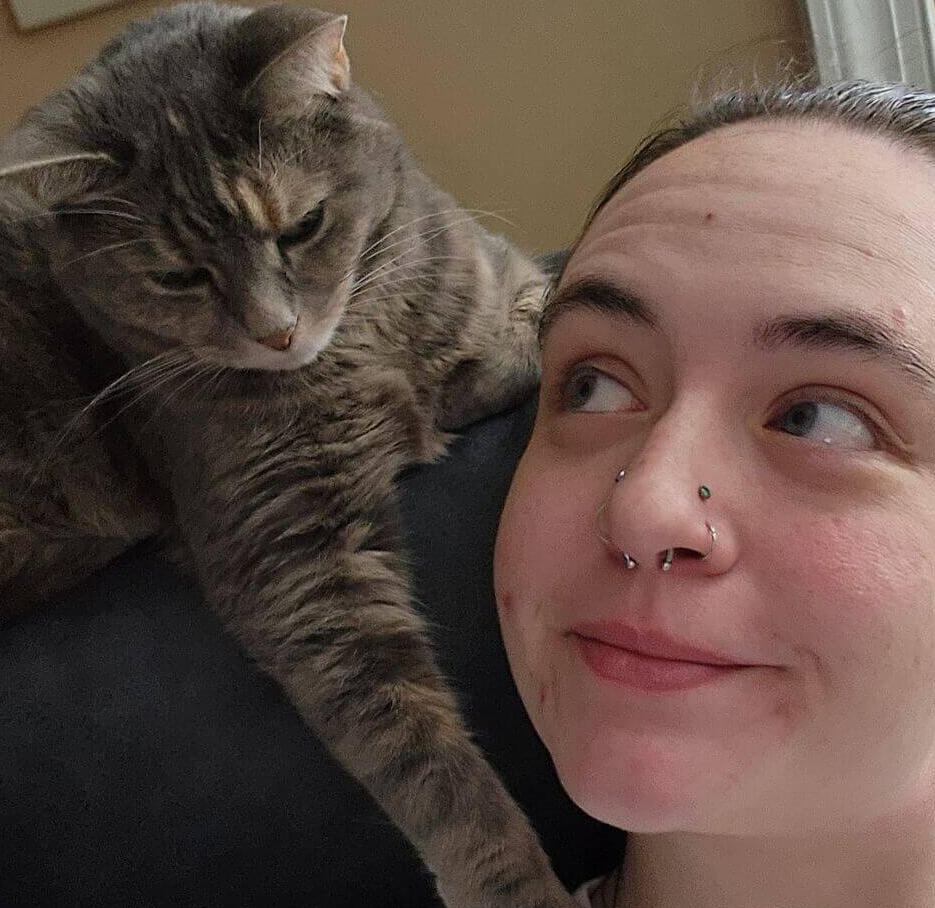 A woman is looking up, smiling, at a grey cat who has her paws on her shoulder.